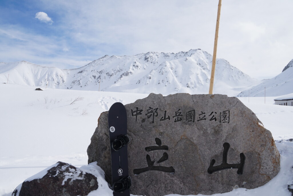 立山(雄山)を奥に見える。立山・中部山岳国立公園の石碑とスノーボード