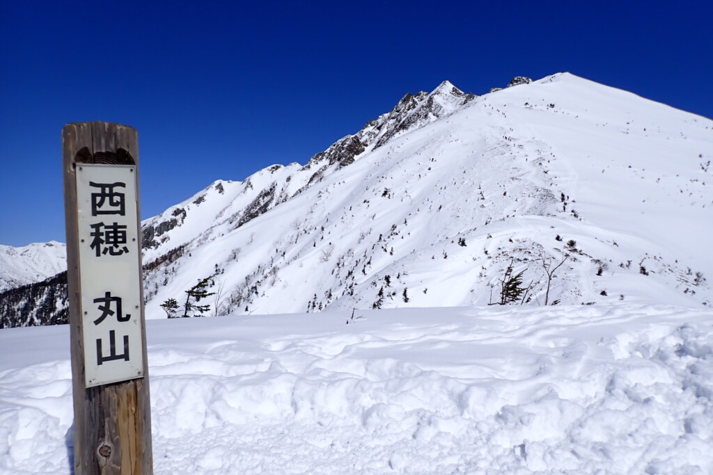 西穂丸山の標識と西穂高岳独標へ続く雪の稜線
