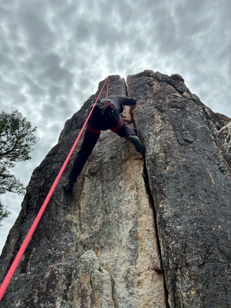 クラックに手足を決めながら岩壁を登るクライマー