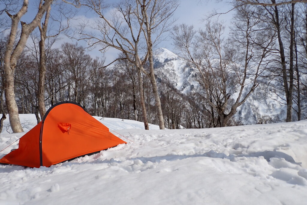 富山県大品山の雪上に設営したオレンジ色のテントと奥に見える鍬崎山