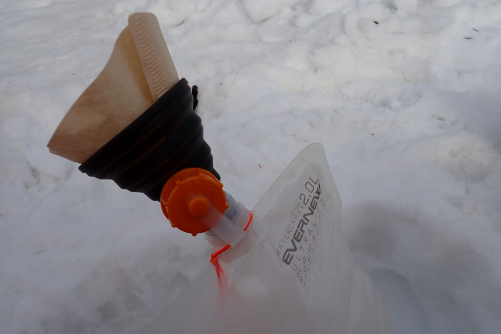雪を溶かした水をコーヒーフィルターと折りたたみ漏斗、小型浄水器でろ過する様子